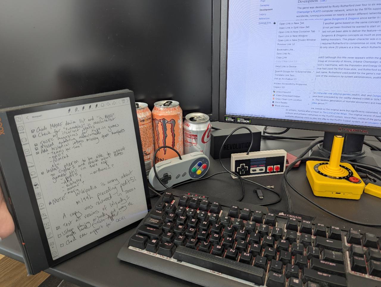 A research desk with handwritten notes, game controllers and historical game research open on a monitor